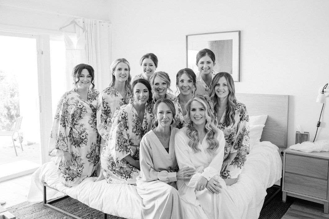 Bridesmaids in floral robes pose with the bride in a bedroom before the wedding.