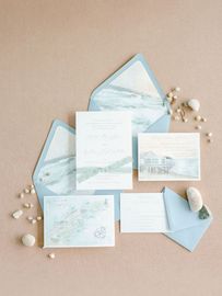 A wedding invitation is sitting on top of a table next to a blue envelope.