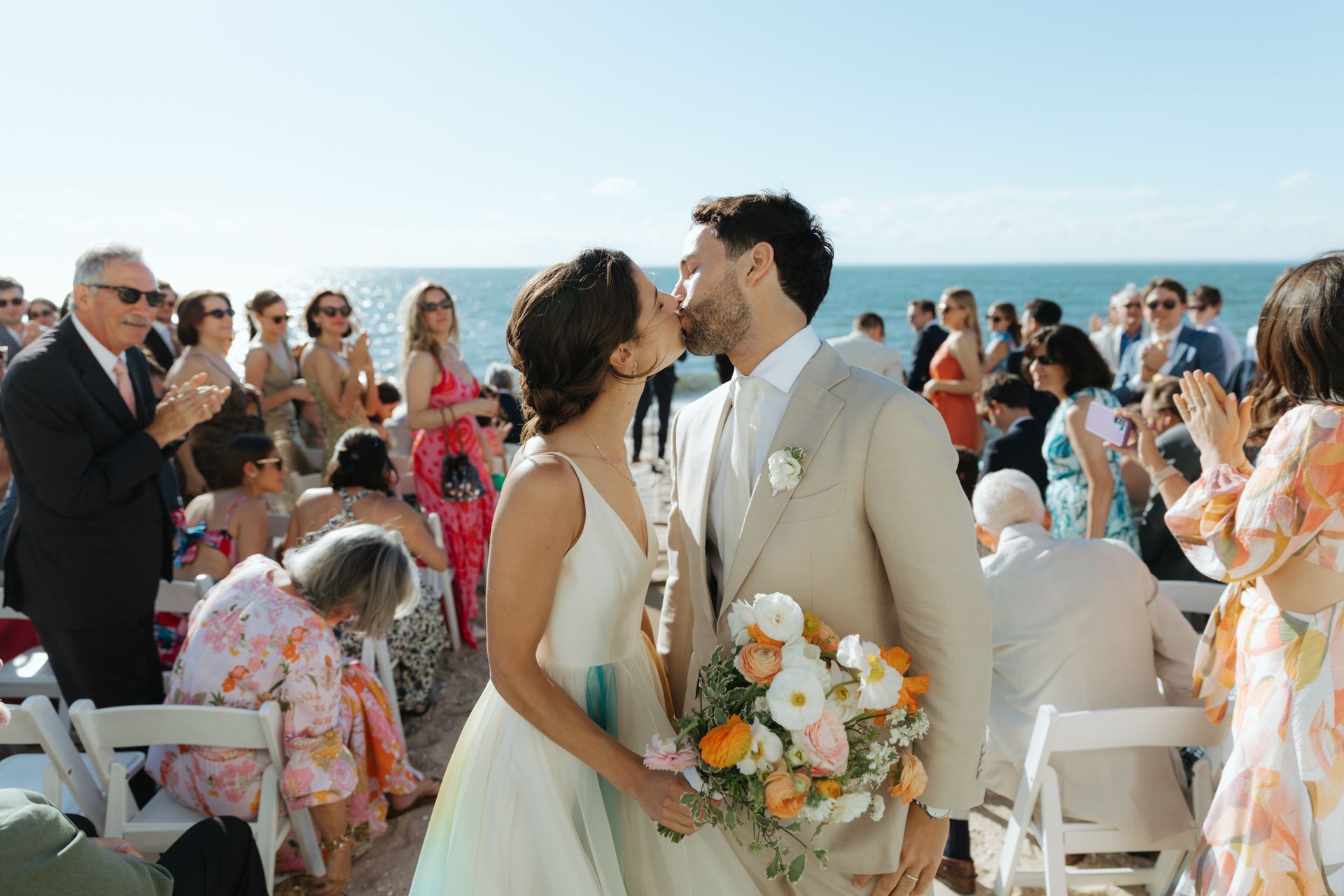 A bride and groom are walking down the beach with their wedding party.