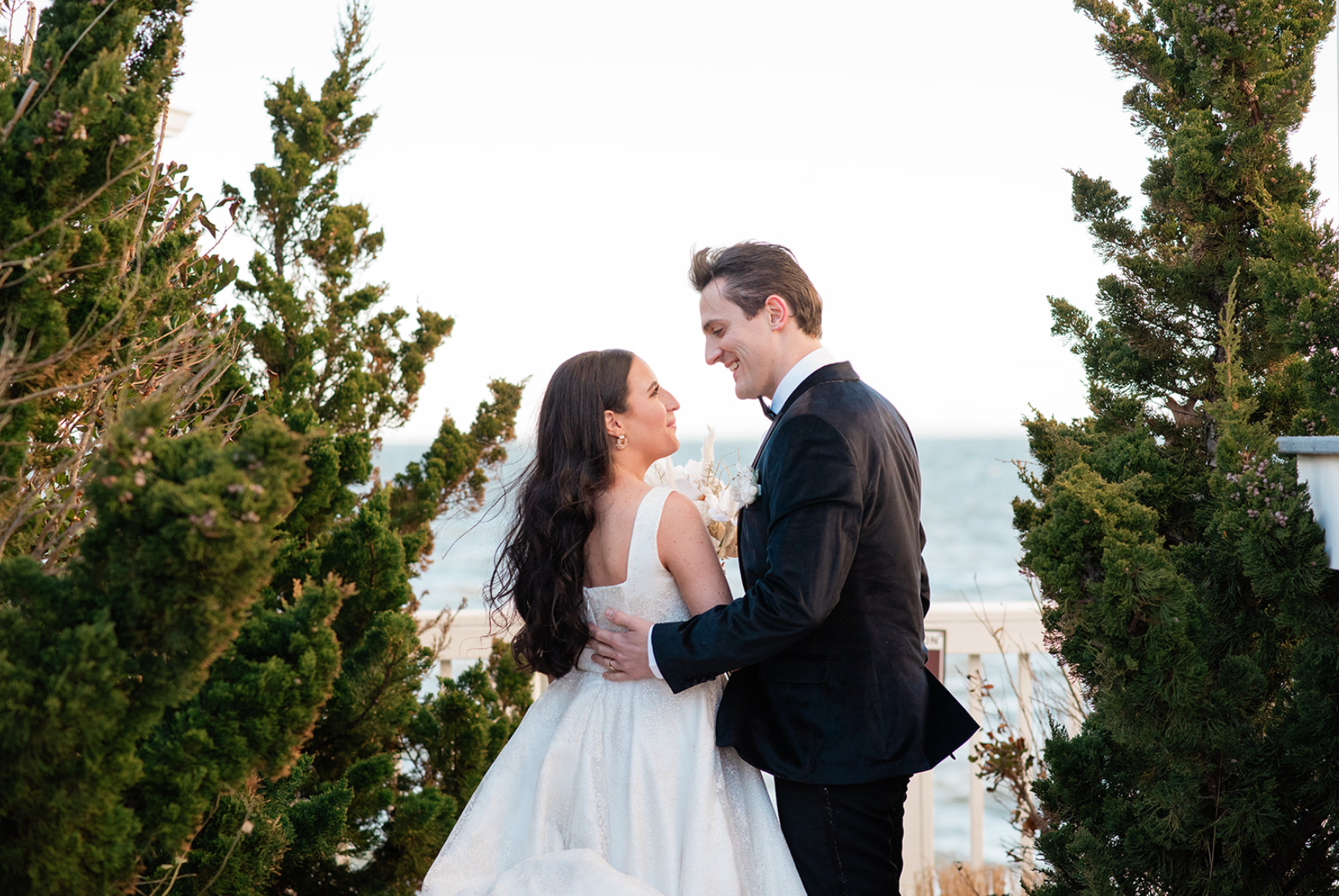 Bride and groom gaze at each other, smiling, with ocean in the background.