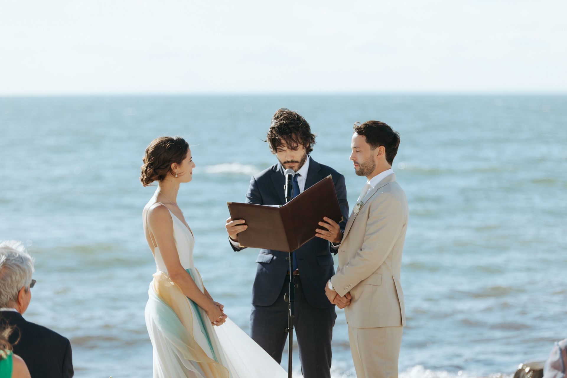 Wedding ceremony on beach; couple, officiant, and ocean in background.