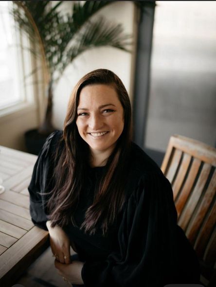 A woman in a black shirt is smiling while sitting at a table.