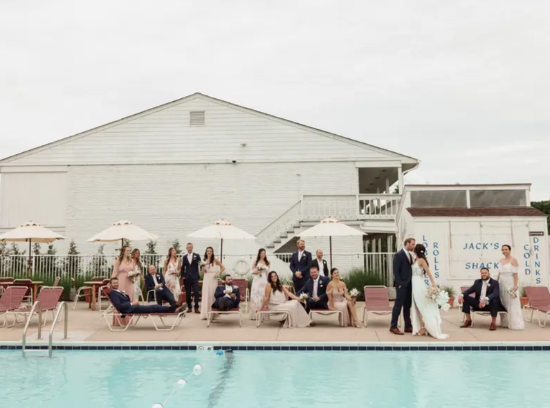 A wedding party is posing for a picture next to a swimming pool.