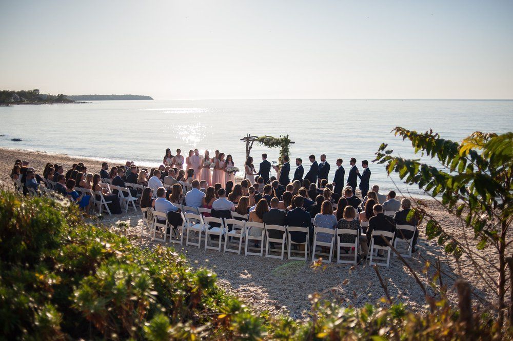 Wedding ceremony on a beach with guests, bridal party, and a wooden arch.