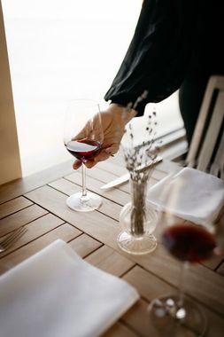 A person is holding a glass of red wine on a table.