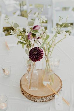 A table with three vases filled with flowers and candles on it.