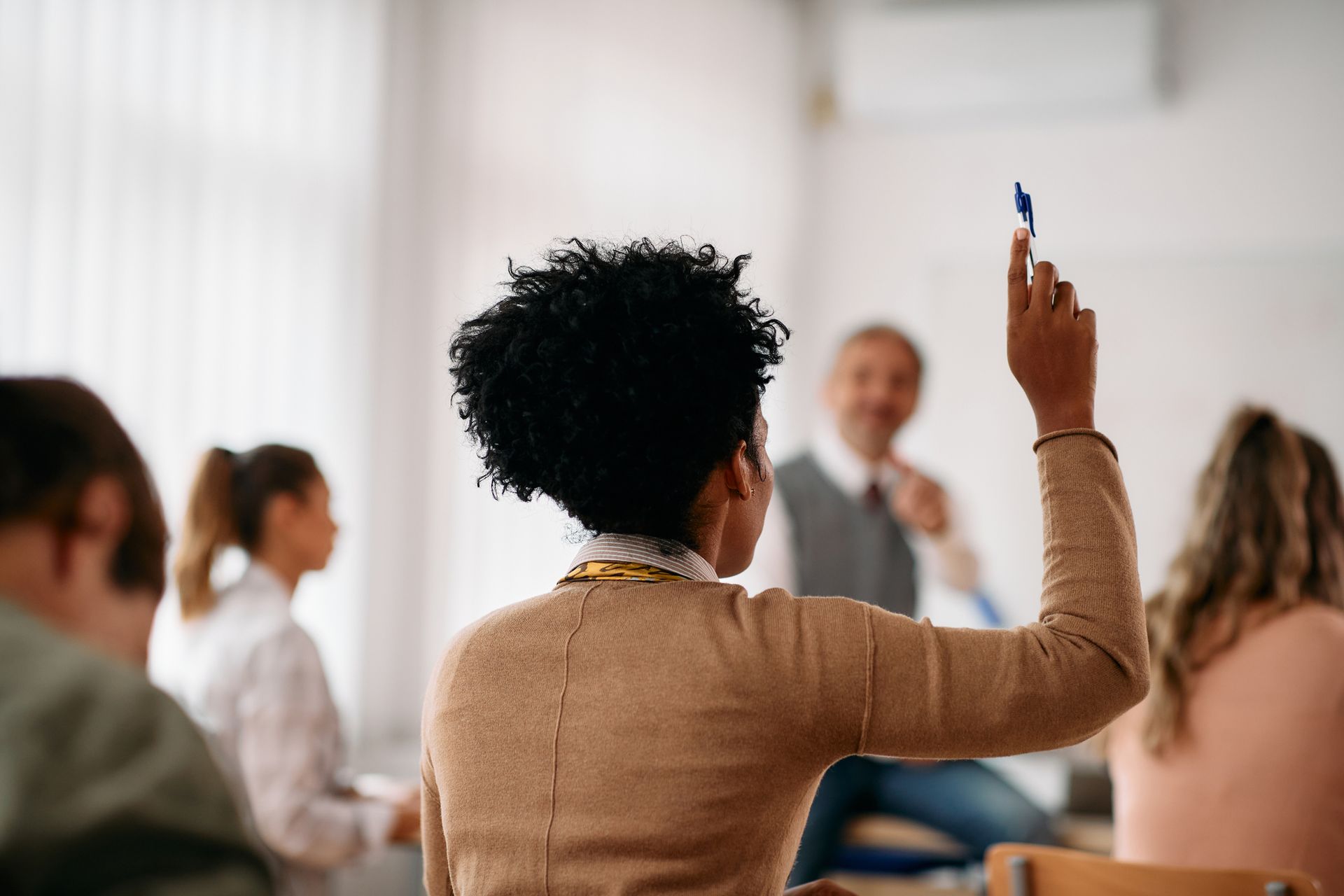 a woman is raising her hand in a classroom to answer a question .