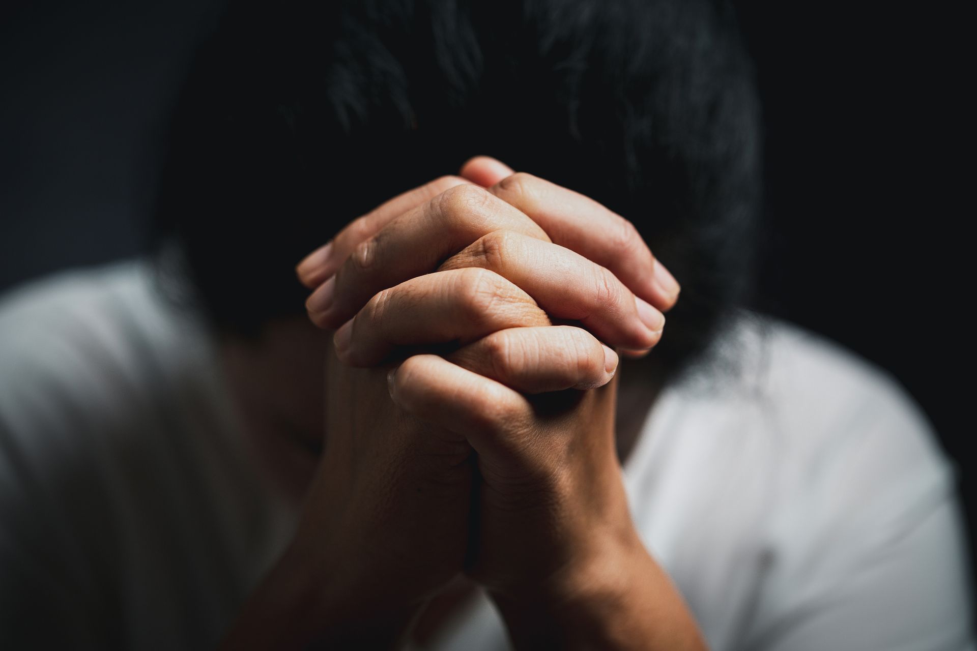 a black and white photo of a man praying with his hands folded in prayer .