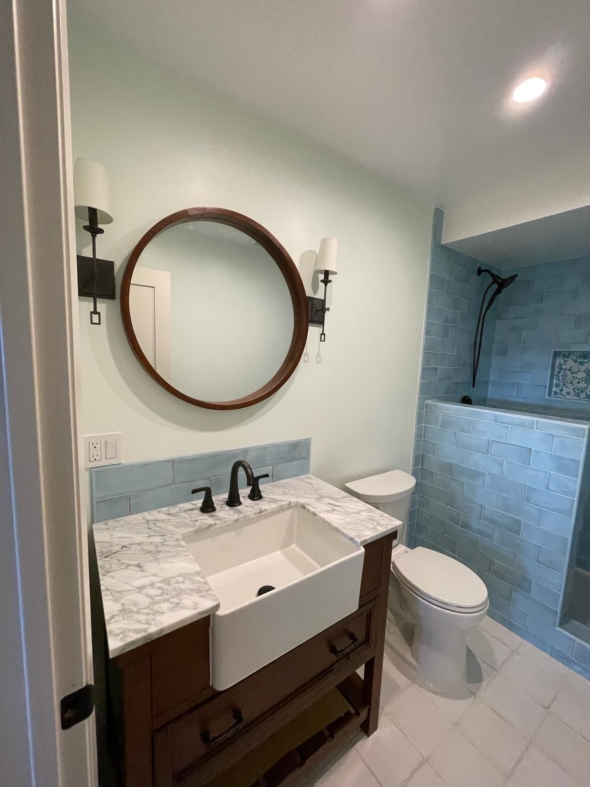 Bathroom with a dark wooden vanity, white sink, and blue-tiled shower.