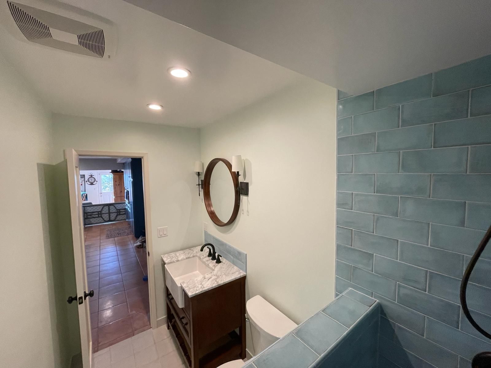 Bathroom with blue tiled shower, vanity, toilet, and mirror. Doorway leads to another room.