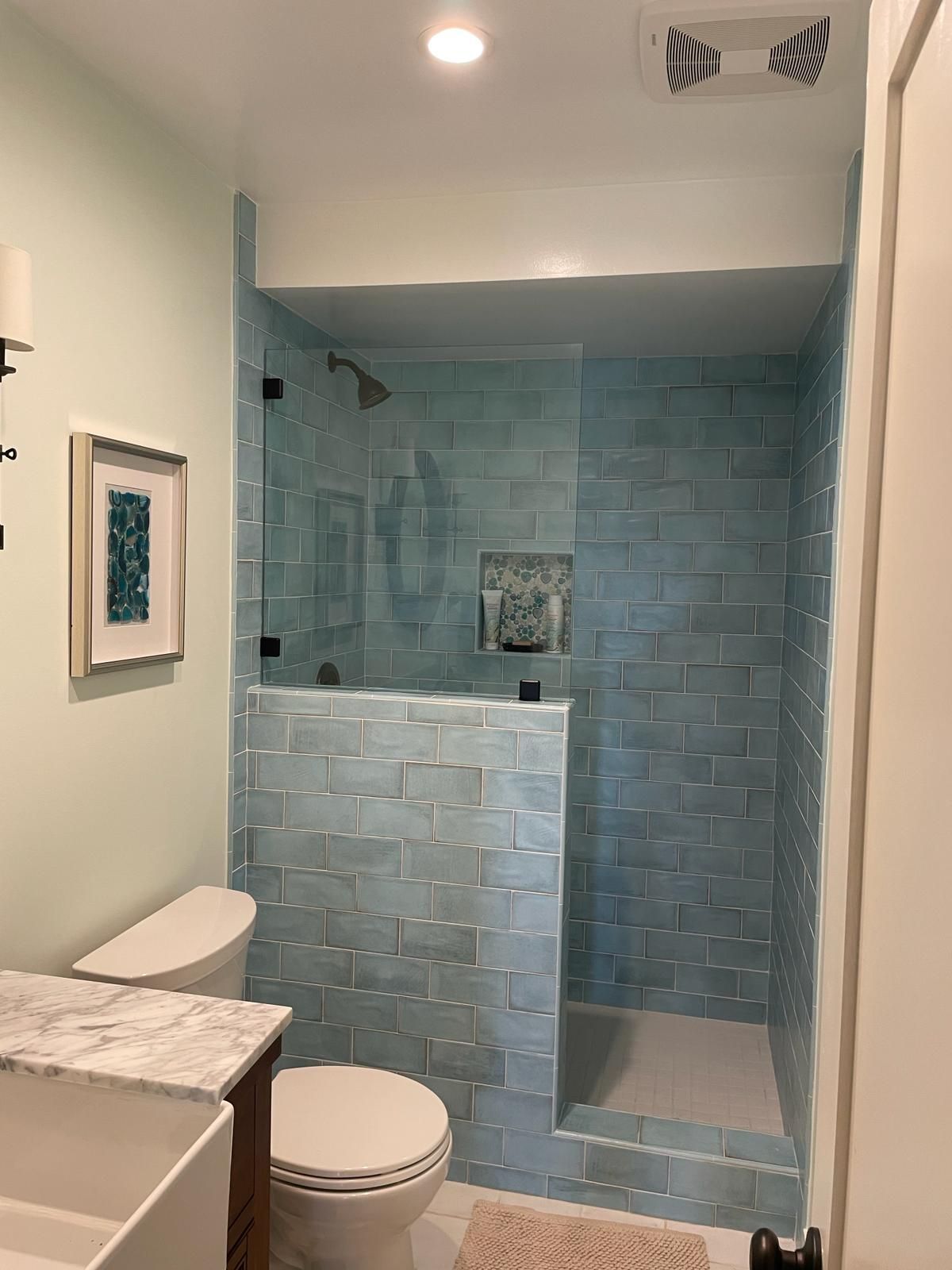 Bathroom with turquoise tiled shower and toilet. Mint green walls, white trim, and a framed picture.