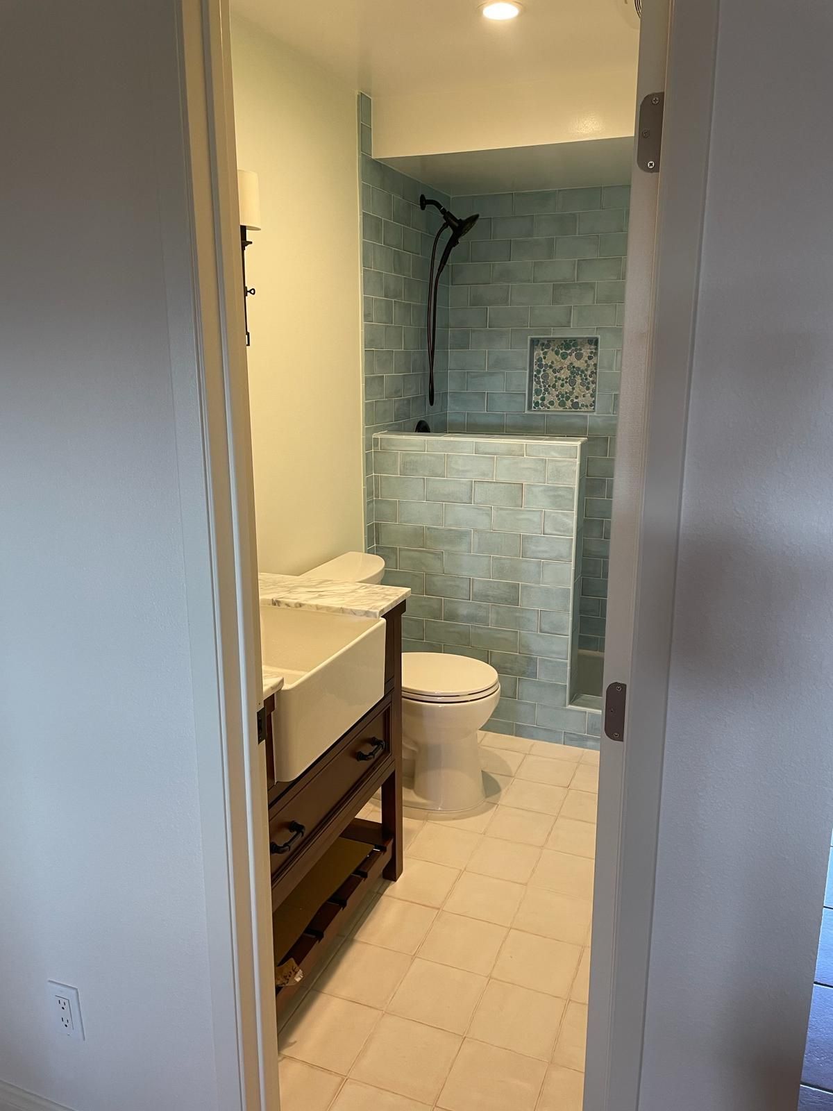 Bathroom interior with blue tiled shower and white toilet and sink.