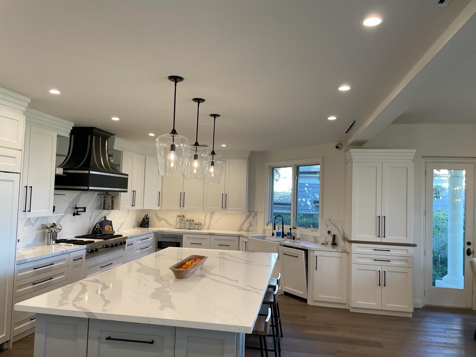 Bright white kitchen with a large island, black accents, and pendant lights.