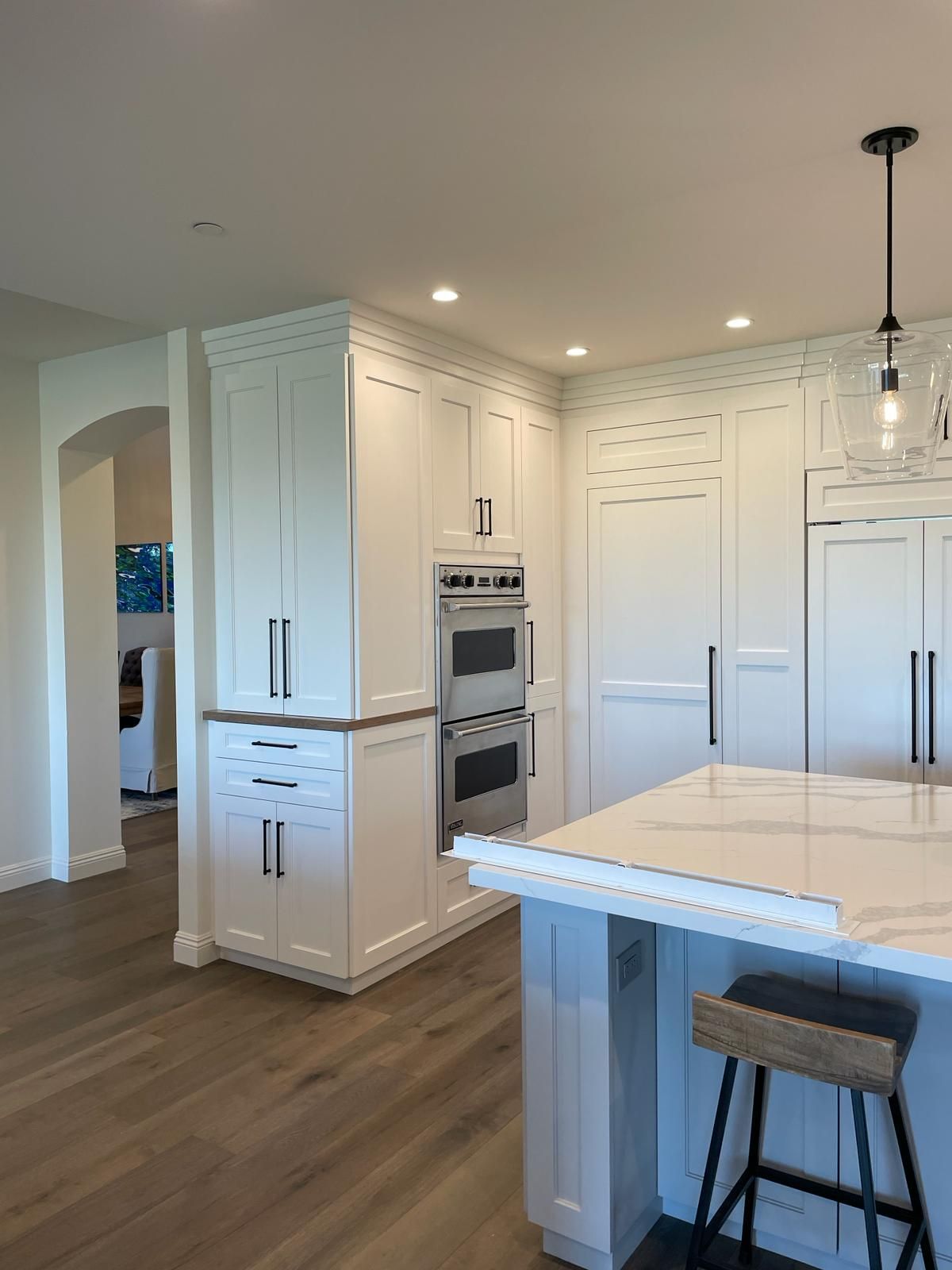 White kitchen with island, cabinets, oven, and hardwood floors.
