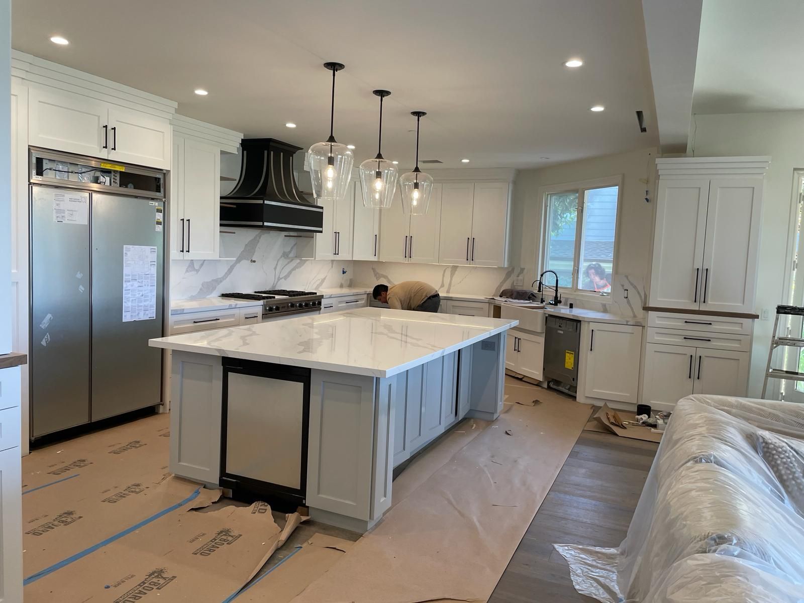 Spacious white kitchen with island, marble countertops, stainless steel appliances, and pendant lights.
