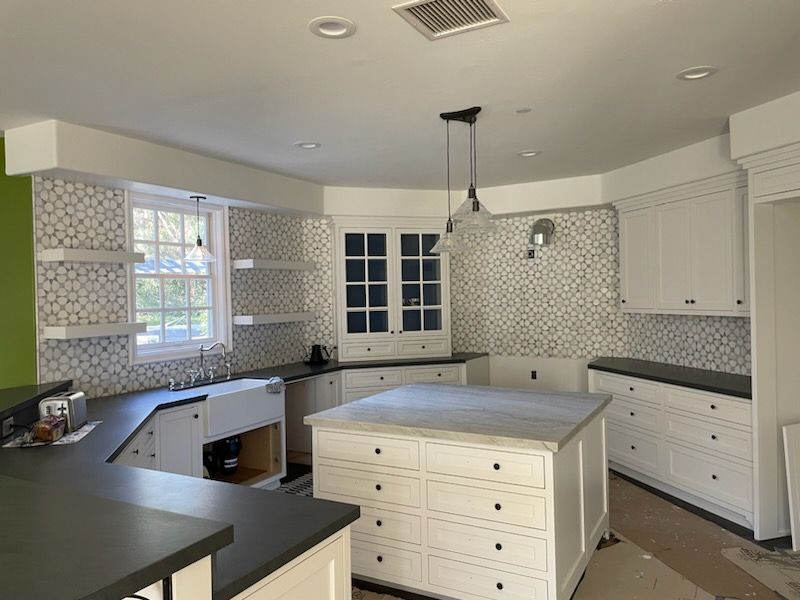 White kitchen under construction with patterned tile backsplash and island with drawers.