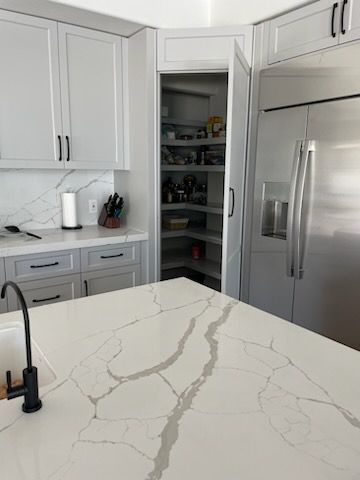 Modern kitchen with a white countertop and a pantry. A stainless steel refrigerator is next to the pantry.