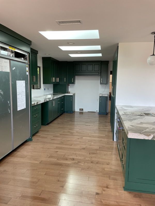 Green kitchen with stainless steel refrigerator, wood floors, and skylights.