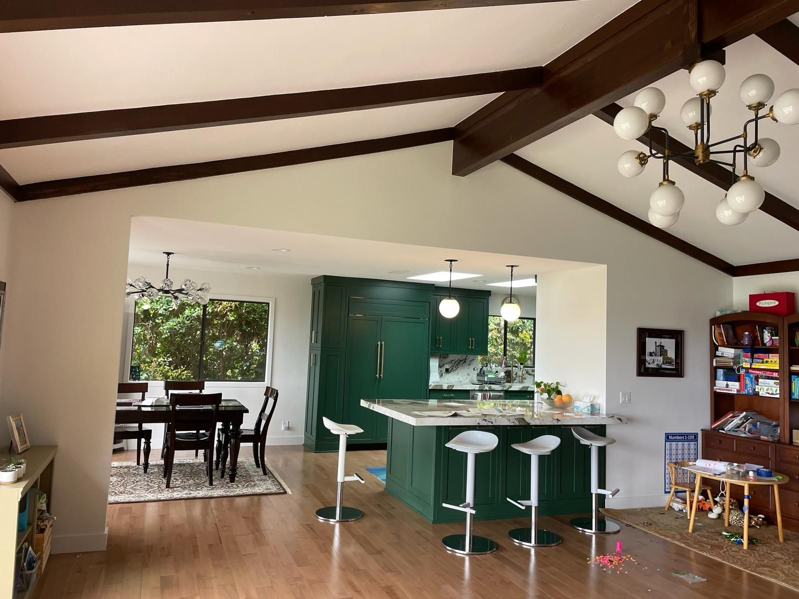Kitchen with green island, white stools, and dark wood beams. Dining area with dark table and chairs visible.