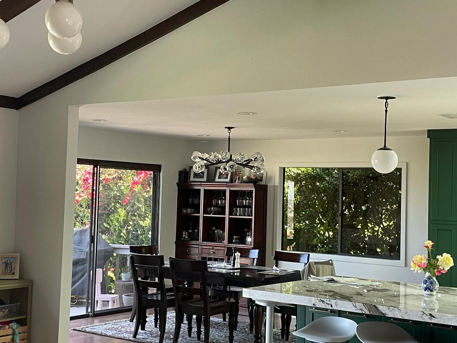 Interior view of a dining area with a table, chairs, and dark cabinets. Sunlight streams in from outside.
