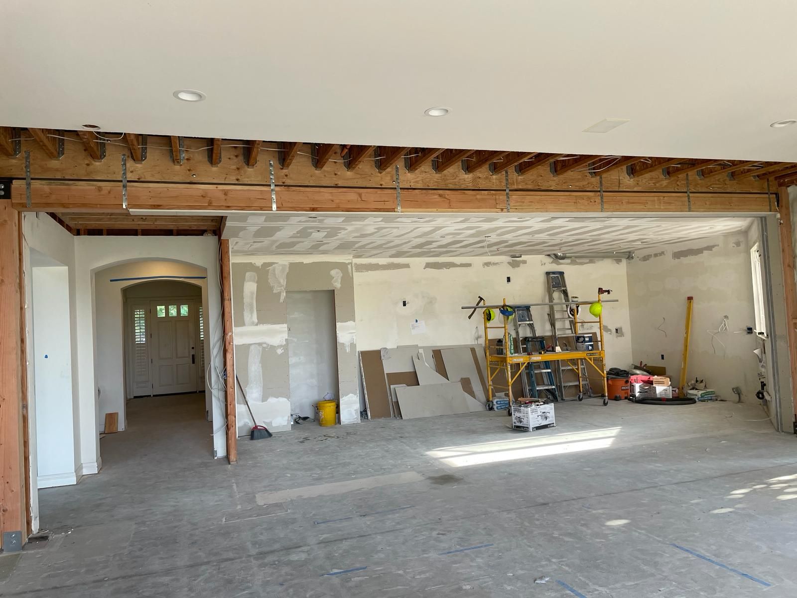 Interior room under construction, showing exposed beams, drywall, and tools.