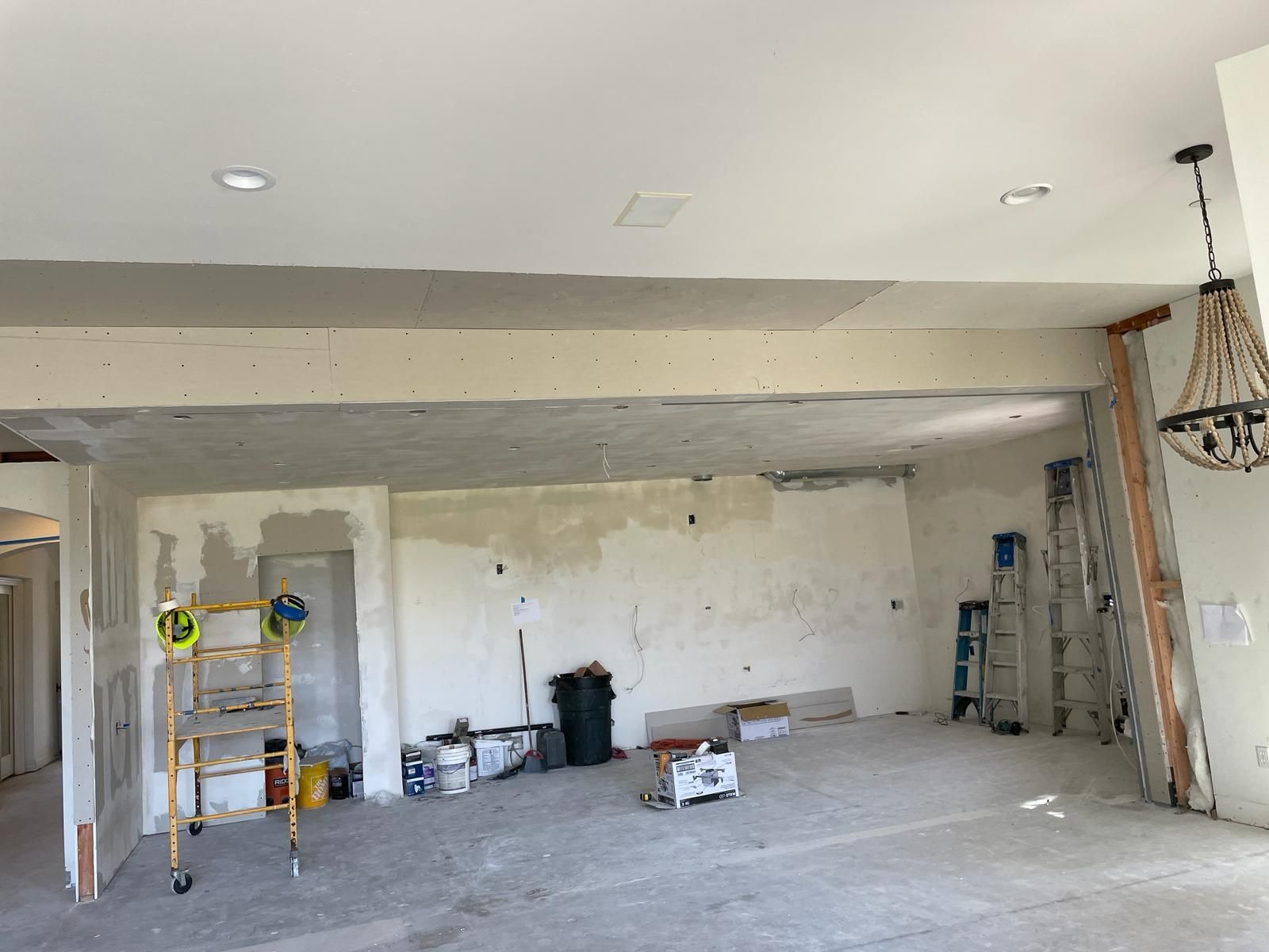 Room under renovation with exposed beams and drywall. Tools and debris litter the floor.