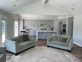 Open-concept living space with two green sofas, kitchen with gray cabinets, and a beige rug.