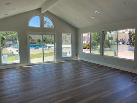 Spacious room with gray walls, wood-look floor, and large windows overlooking a pool.