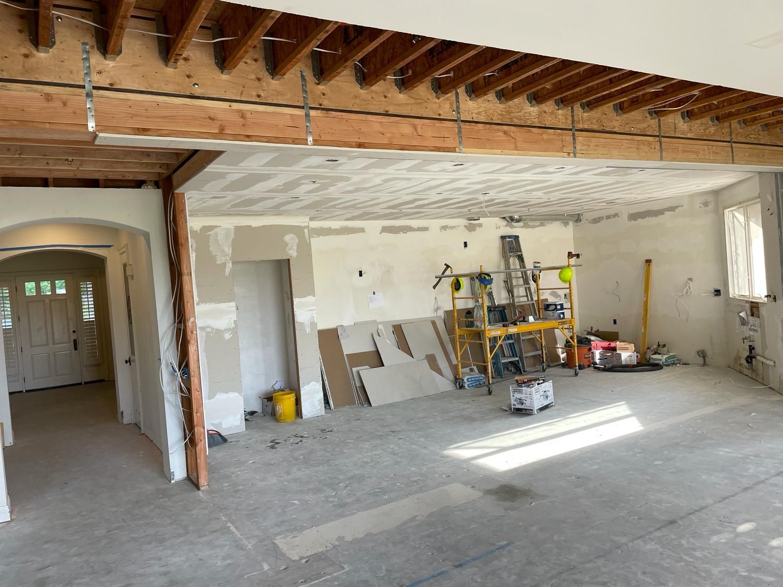 Interior construction site, drywall walls and exposed ceiling beams, tools and materials scattered, natural light.