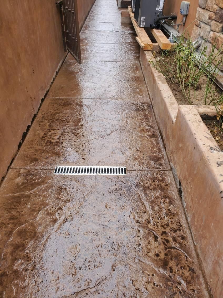 Narrow concrete walkway with decorative brown finish, a drain, and bordering walls.
