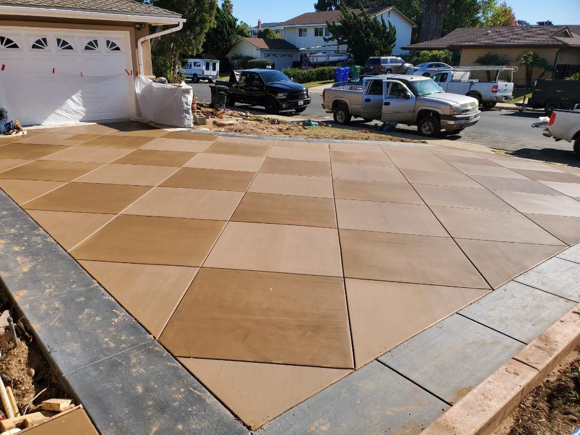 Driveway paved with checkerboard pattern tiles in shades of brown. Cars parked in background.