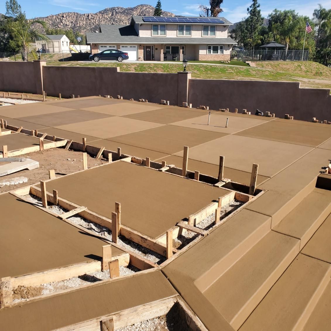 Concrete work in progress, with forms and poured sections, near a two-story house.