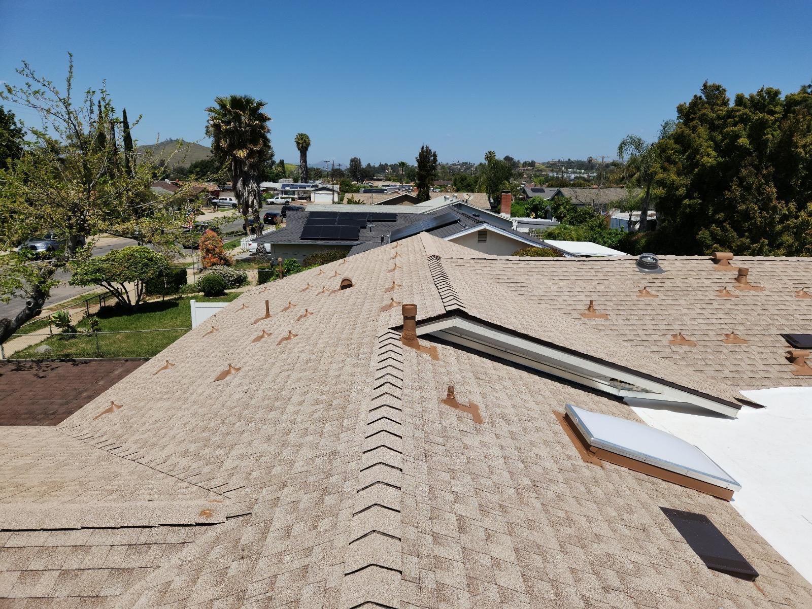 View of a residential rooftop with newly installed shingles, skylights, and a bright blue sky in the background.