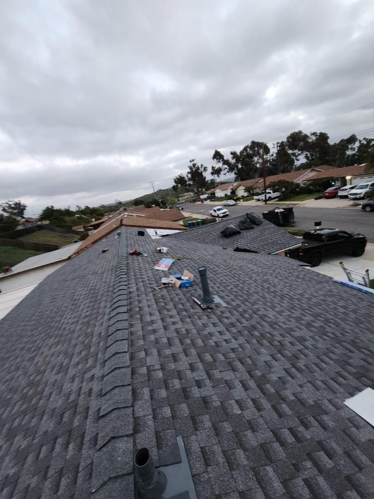 Gray asphalt shingle roof, cloudy sky, residential neighborhood in background.
