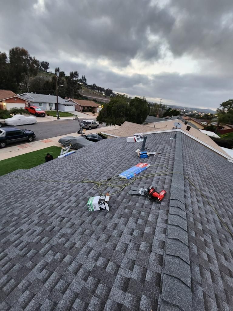 Rooftop with asphalt shingles and tools. Cloudy sky, suburban street in background.