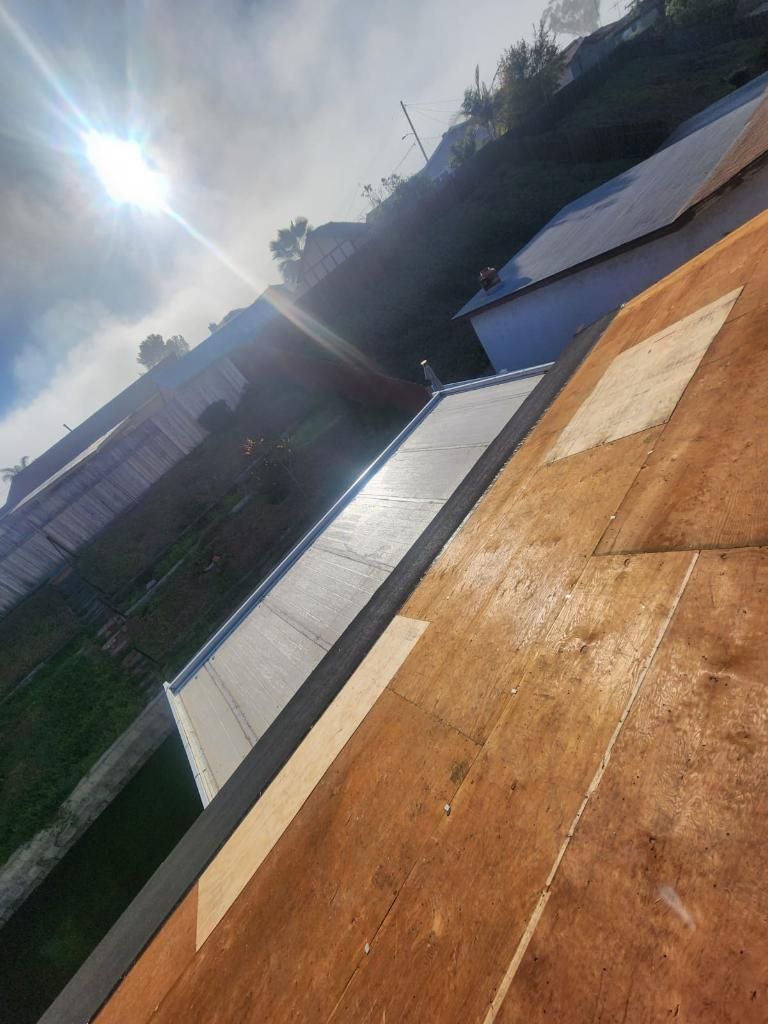 Sun shining over rooftops, a grassy area, and a building on a hillside.