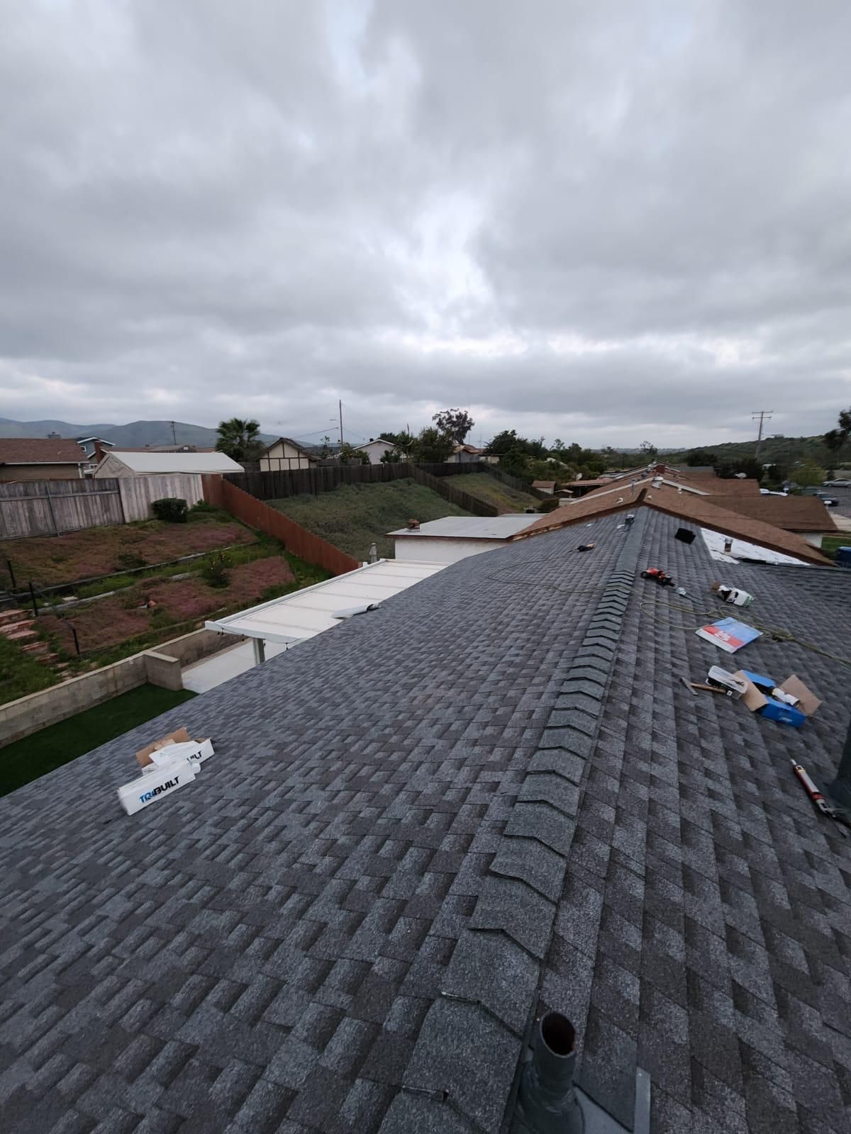 Gray shingle roof, cloudy sky, view of residential neighborhood with homes and vegetation.