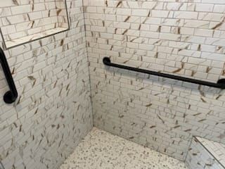 Shower stall with marble-patterned tile, black grab bar and a built-in shelf. The floor has a speckled pattern.
