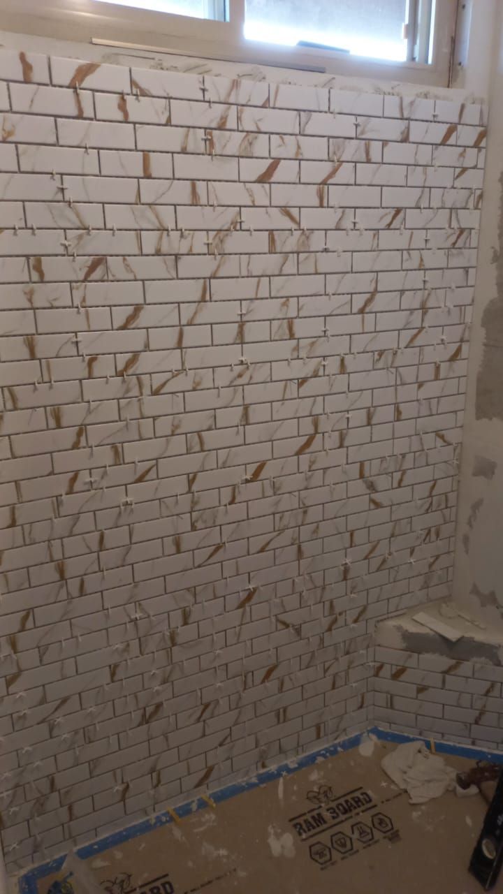 Bathroom wall under construction, white brick tile with brown veining pattern, near a window.