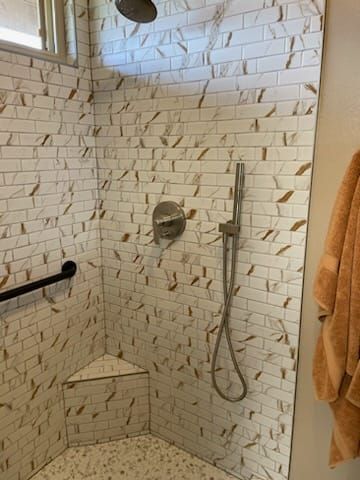 Shower with white and brown tile, grab bar, showerhead, and a towel hanging nearby.