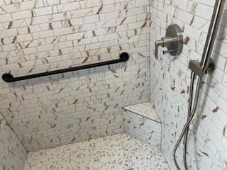 Shower stall with white and brown tile, black grab bar, and step-up bench.
