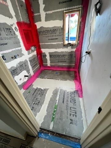 Bathroom renovation in progress; gray cement board walls with pink waterproofing.