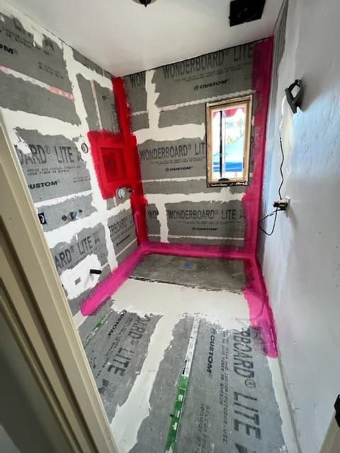 Bathroom under construction: waterproof membrane applied around walls and floor, shower area defined in pink.