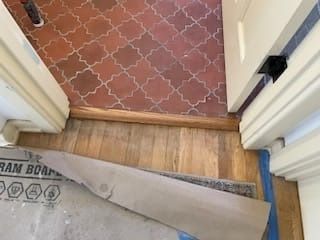 Doorway with terracotta tile floor and wood flooring, trim visible.