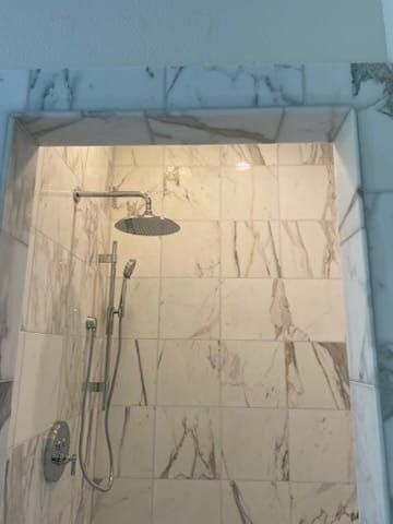 Shower with marble-like tile and chrome fixtures, including a rain shower head and handheld sprayer.