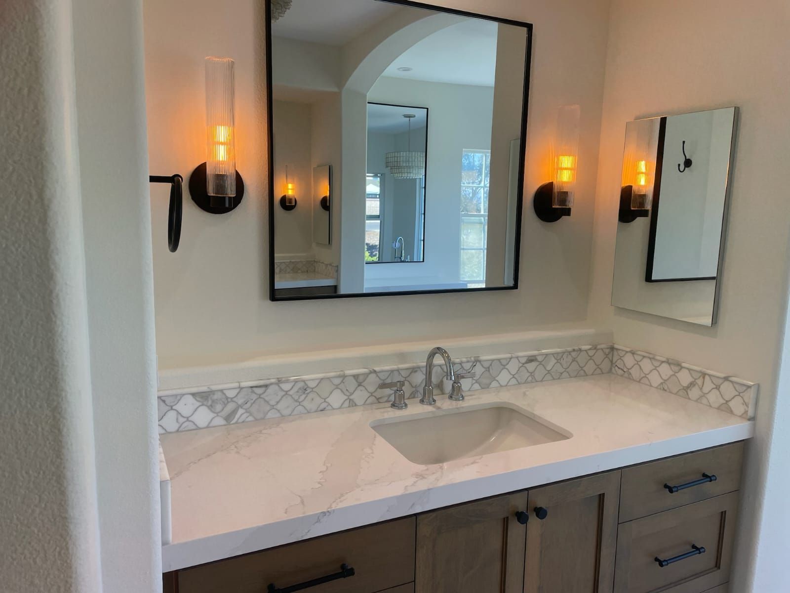Bathroom vanity with marble countertop, sink, mirror, sconces, and wooden cabinets.