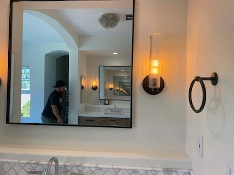 Bathroom with mirror reflecting a man, sconce lighting, and towel ring.