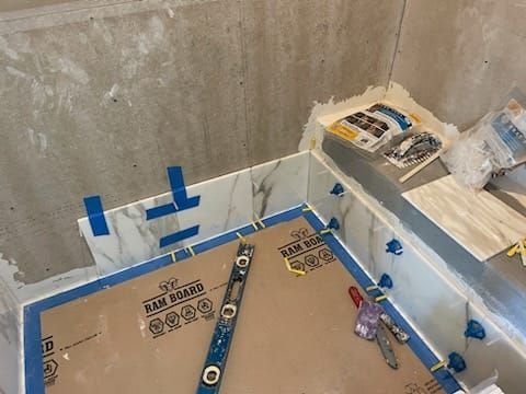 Tiling in progress: White marble-look tiles on a countertop, blue tape, level, tile spacers, and tools.