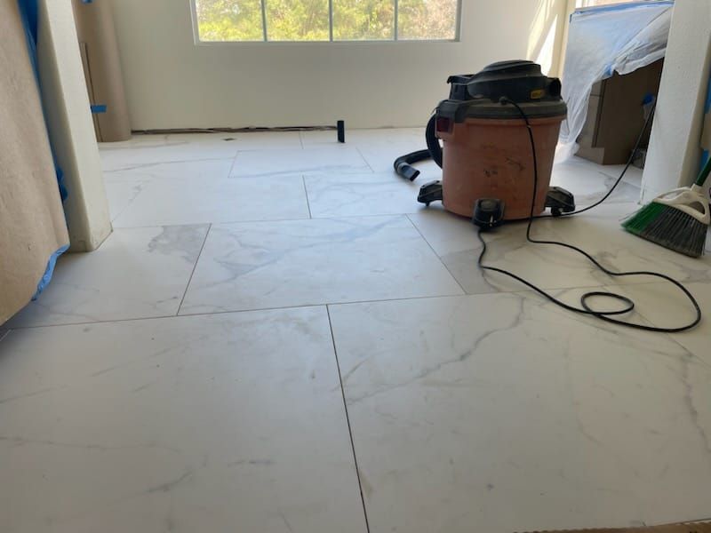 White tile floor in a room under construction, with a shop vacuum and window in the background.