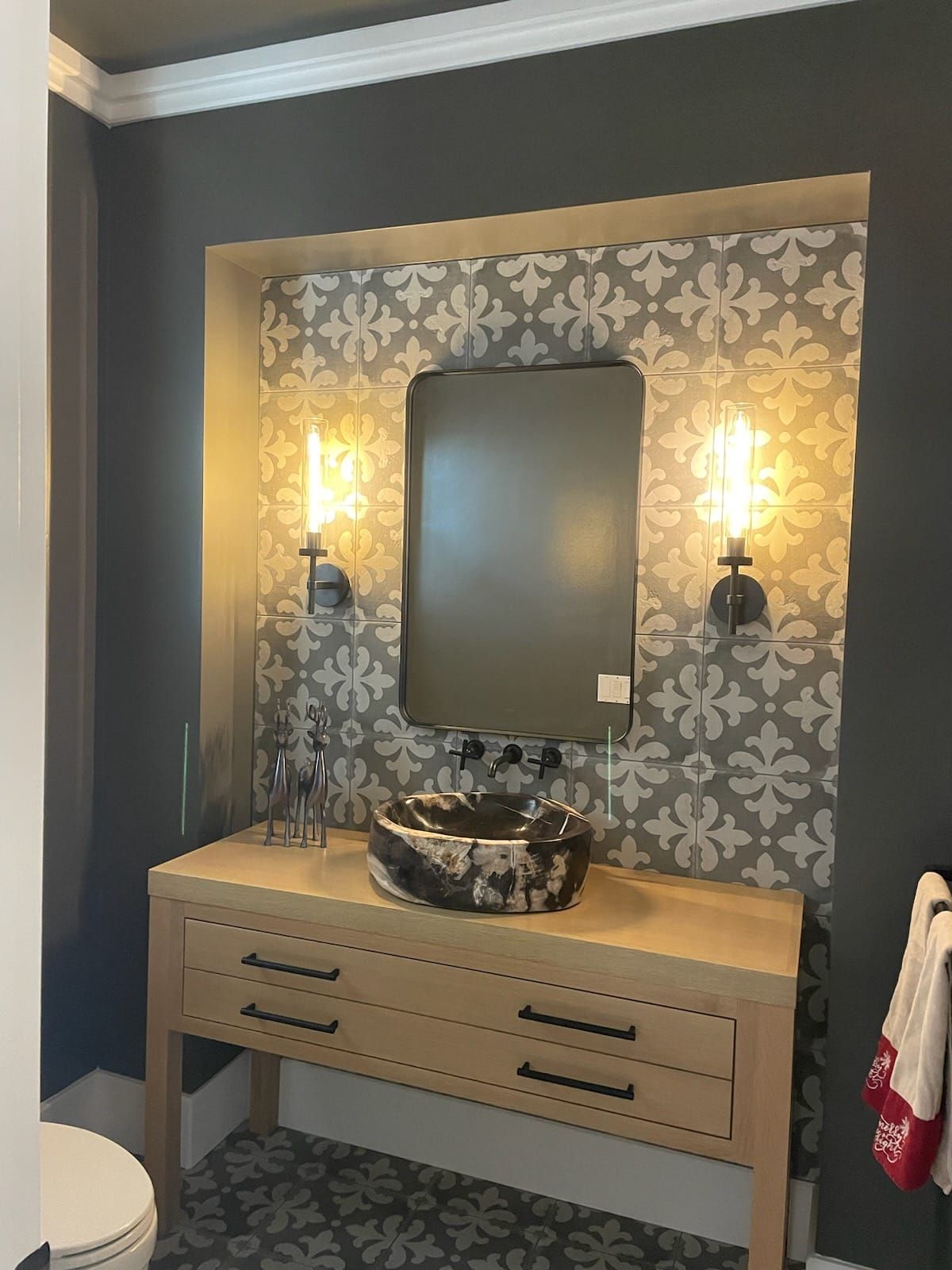 Vanity area with a wooden cabinet, patterned sink and backsplash, and a large mirror flanked by lights.